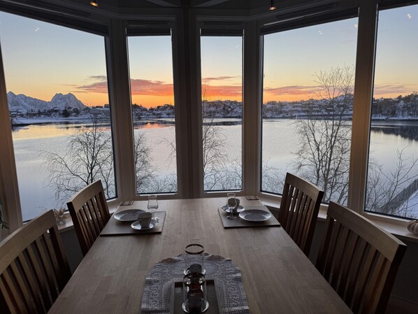 A dining table with chairs, a placemat, and a view of a lake and mountains at sunset.