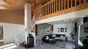 A spacious living area with a wooden staircase, a black leather sofa, a coffee machine, and a large plant. - Lofoten Villa by the sea (Vågan)