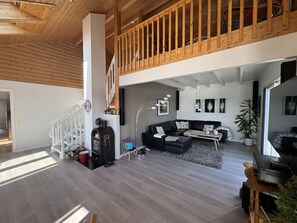 Un vaste espace de vie agrémenté d’un escalier en bois, d’un canapé en cuir noir, d’une machine à café et d’une grande plante.