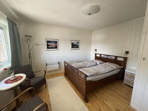 Una camera da letto con un letto di legno, un tavolino con un vaso, una sedia, una lampada da terra e due quadri appesi al muro.