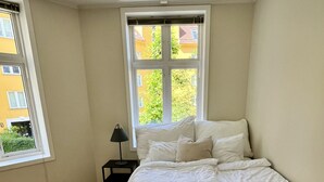 A bedroom with a large bed, a nightstand, a lamp, and a window with a view of buildings. - Central apartment close to Bryggen (Bergen)