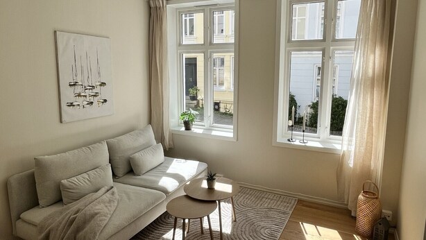 A living room with a sofa, a small table, a rug, and large windows with curtains. - Central apartment close to Bryggen (Bergen)