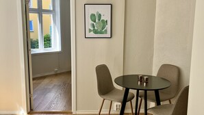 A room with a wooden floor, a round table with chairs, a framed picture on the wall, and a door leading outside. - Central apartment close to Bryggen (Bergen)