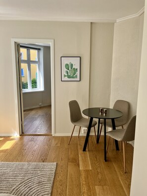 Ein Zimmer mit Holzboden, einem runden Tisch mit Stühlen, einem gerahmten Bild an der Wand und einer Tür, die nach draußen führt.