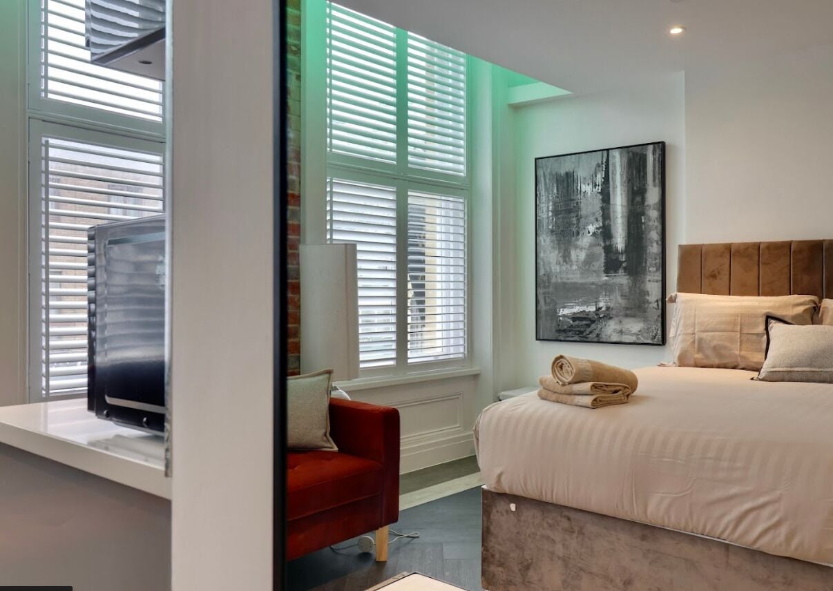 A modern bedroom with a bed, a red chair, a television, and a large window with blinds.