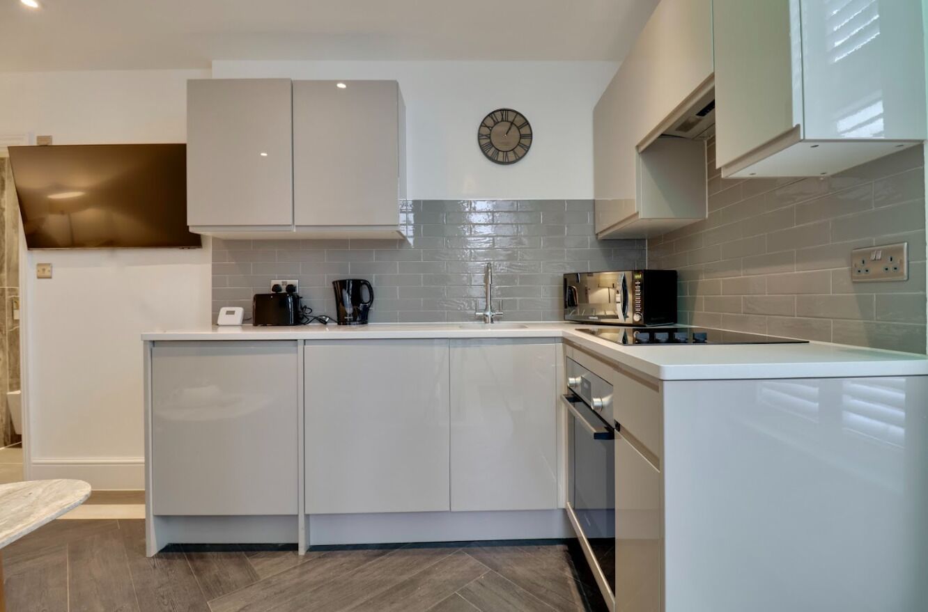 Une cuisine moderne avec des meubles blancs, un four à micro-ondes, une machine à café et une horloge au mur.