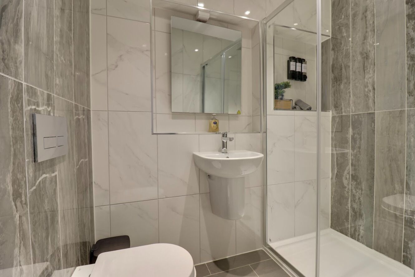 A modern bathroom with a marble wall, a white sink, a mirror, and a glass shower enclosure.
