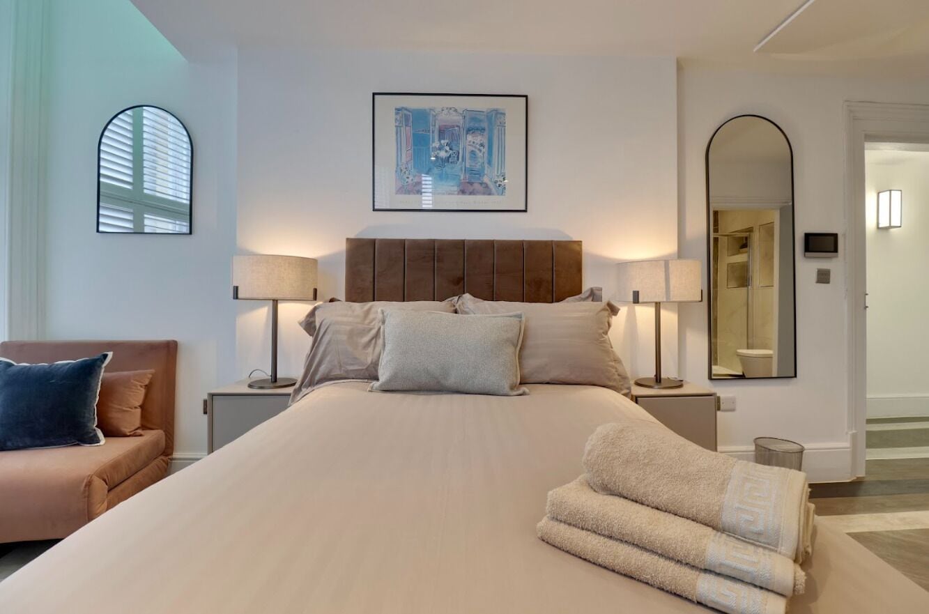 A bedroom with a large bed, two bedside lamps, a mirror, and a framed picture on the wall.