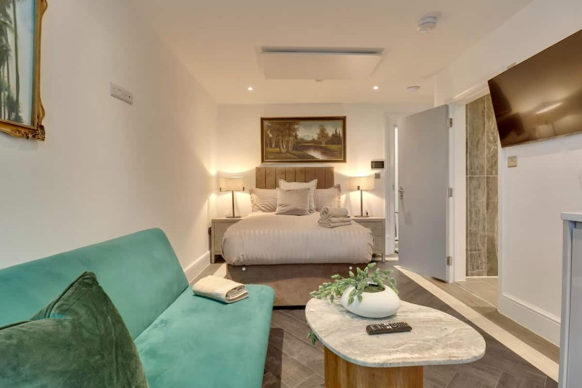 A hotel room with a bed, a green sofa, a small table with a plant, and a TV on the wall.