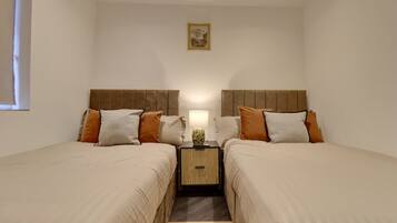 A double room with two beds, a nightstand with a lamp, and a small painting on the wall.