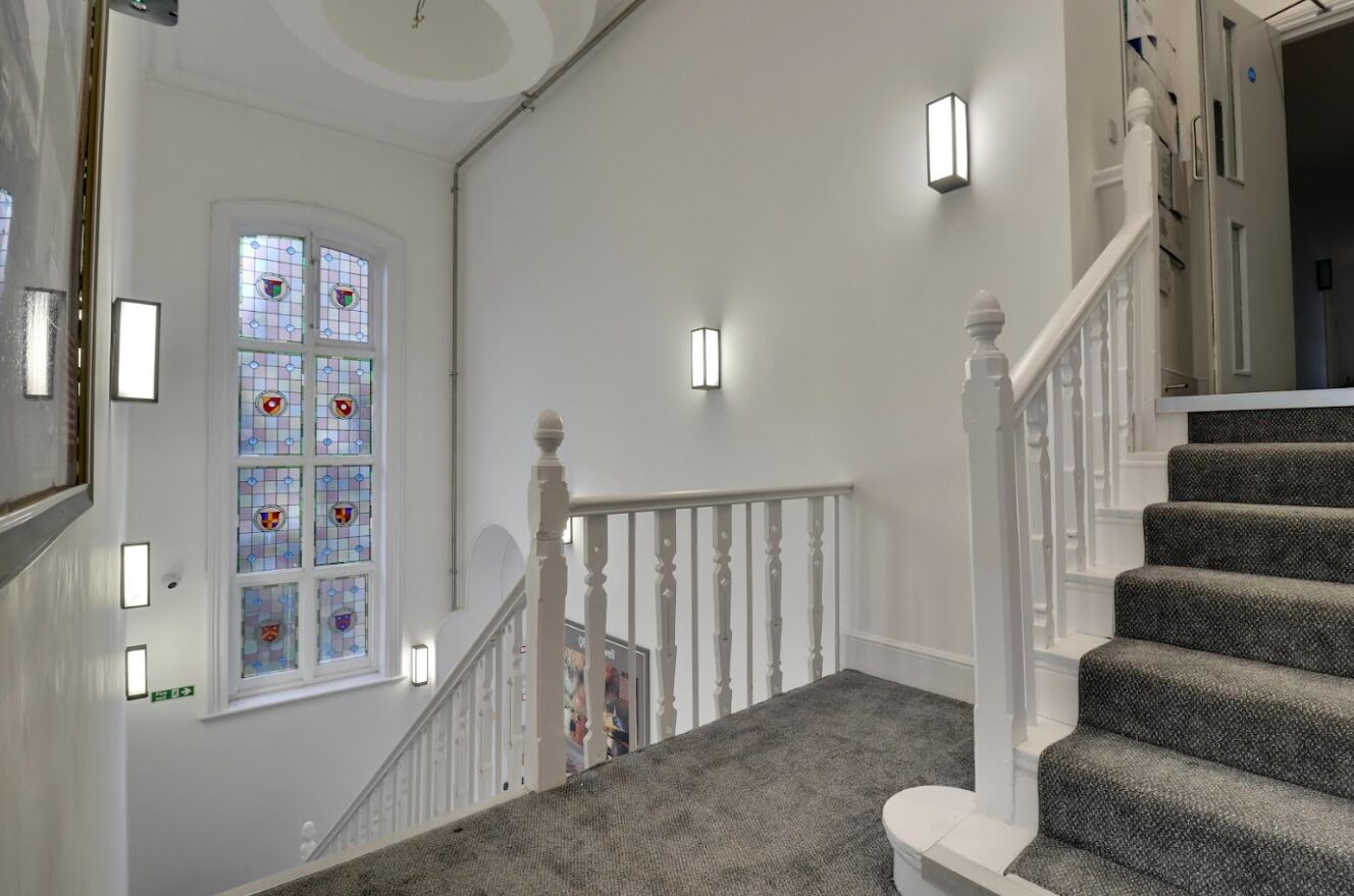 A staircase with white balusters, a carpeted landing, and a stained glass window with colorful designs.