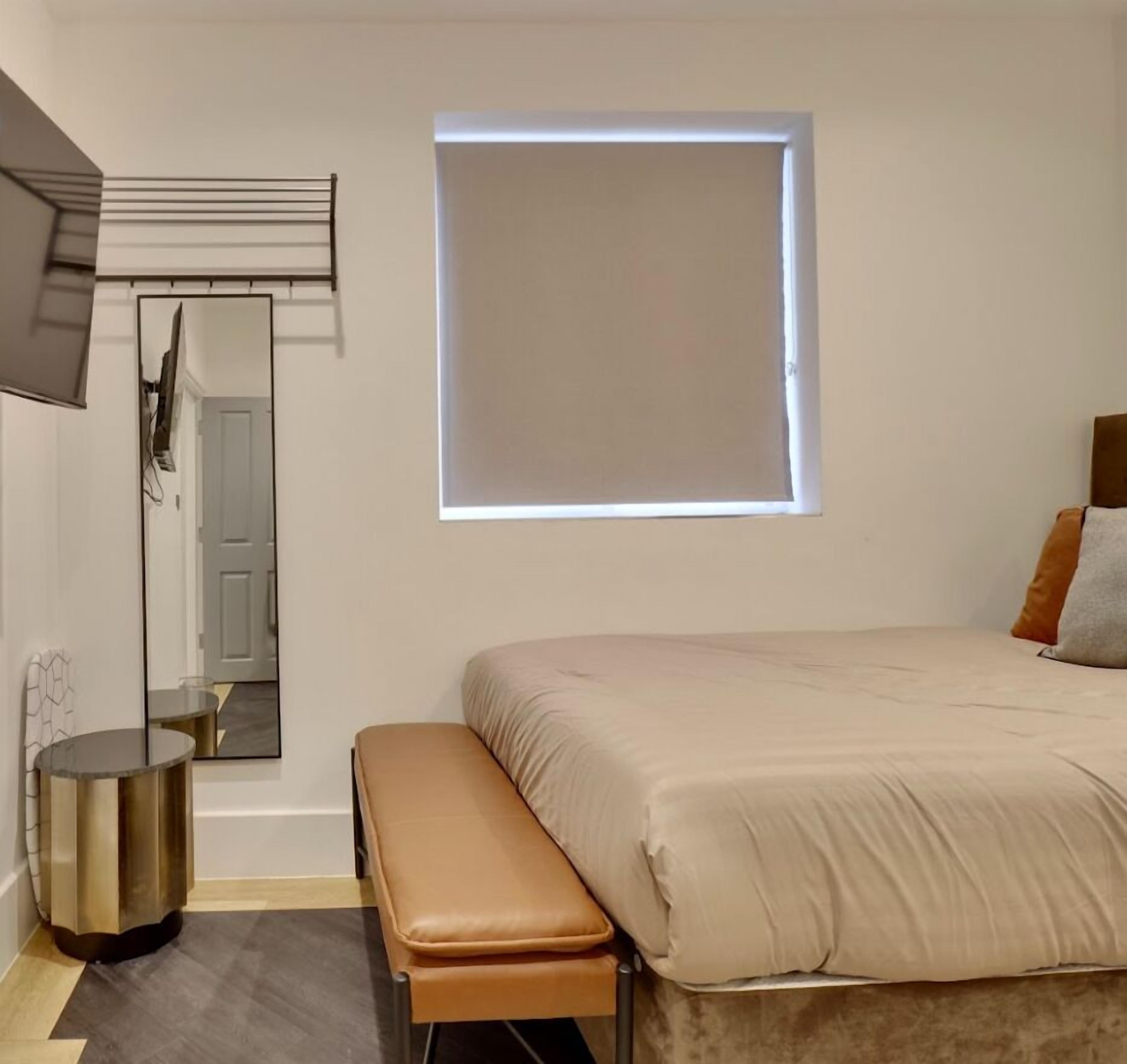 Une chambre à coucher avec un lit, un banc, un miroir, une fenêtre et une porte.