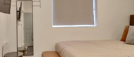 Une chambre à coucher avec un lit, un banc, un miroir, une fenêtre et une porte.