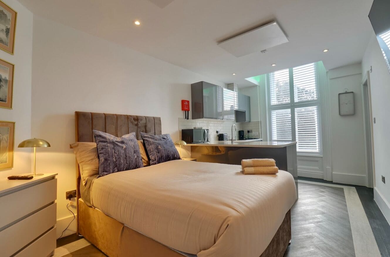 A modern bedroom with a large bed, bedside tables, a built-in desk, and a view of the outdoors through large windows.