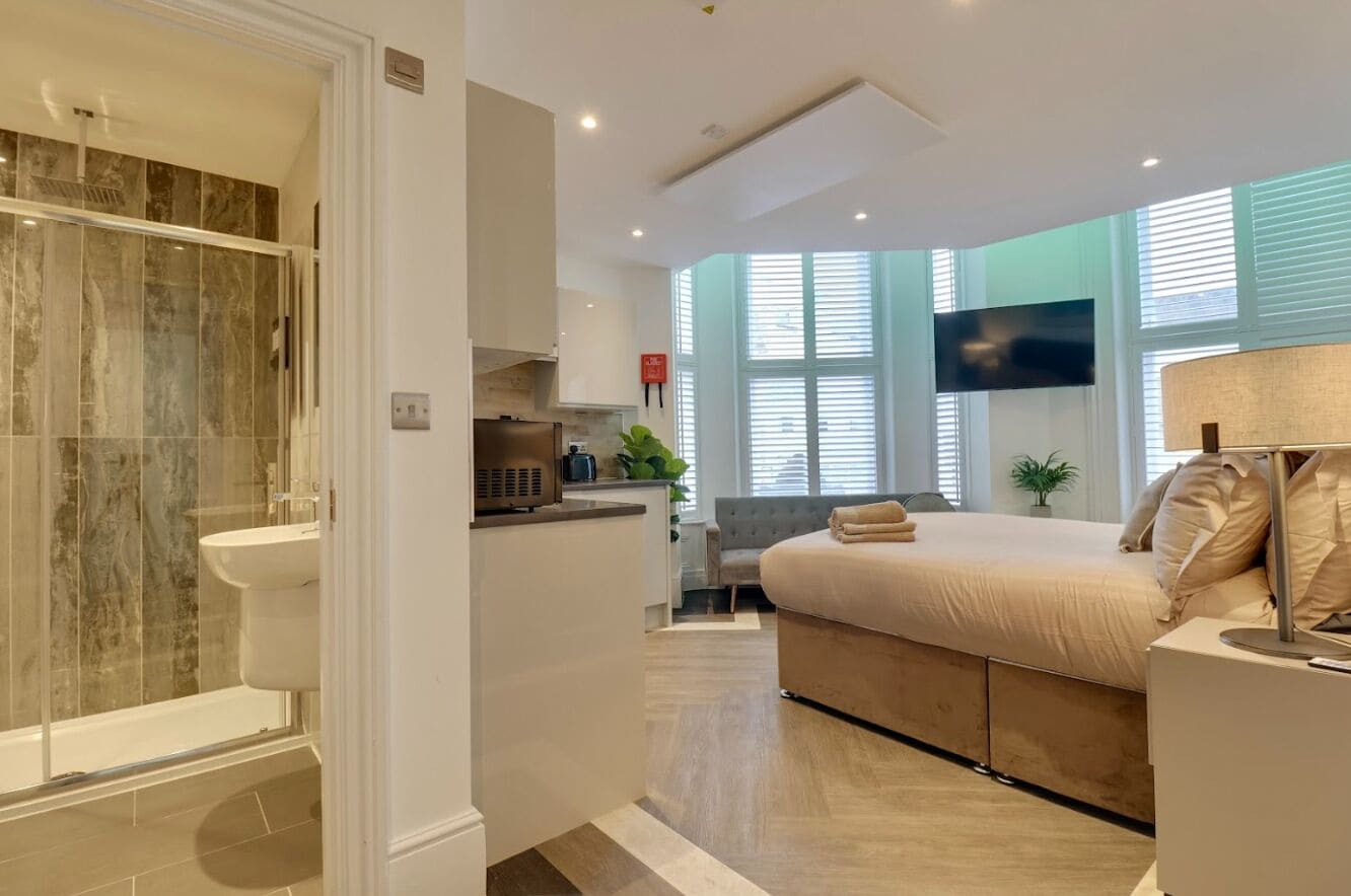 A modern bedroom with a large bed, a TV, and a bathroom with a shower and sink.
