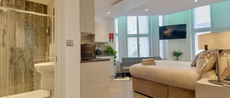 A modern bedroom with a large bed, a TV, and a bathroom with a shower and sink.