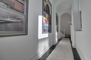 A hallway with framed pictures on the walls, a tiled floor, and a staircase leading to another level. - QE2 Loft Apartments (Southampton)