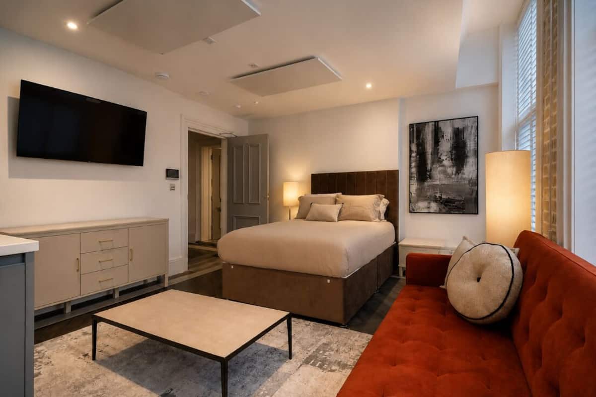 A modern bedroom with a bed, a TV, a sofa, and a painting.