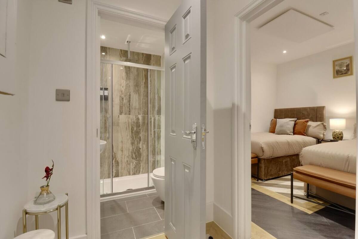 A hotel room with a shower, toilet, bed, bedside table, and a vase with a flower.