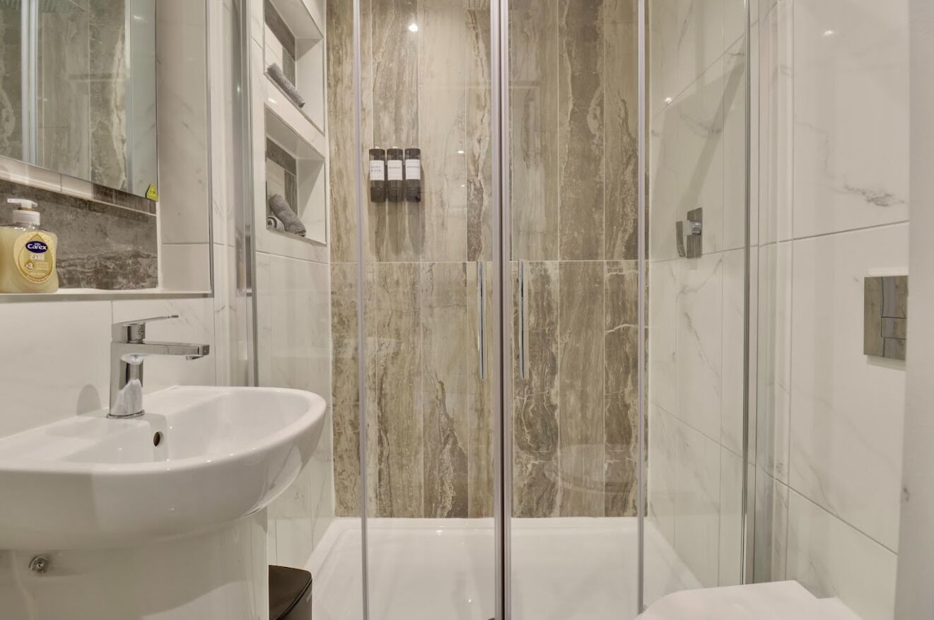 Un baño moderno con ducha de vidrio, lavabo blanco y salpicadero de mármol.