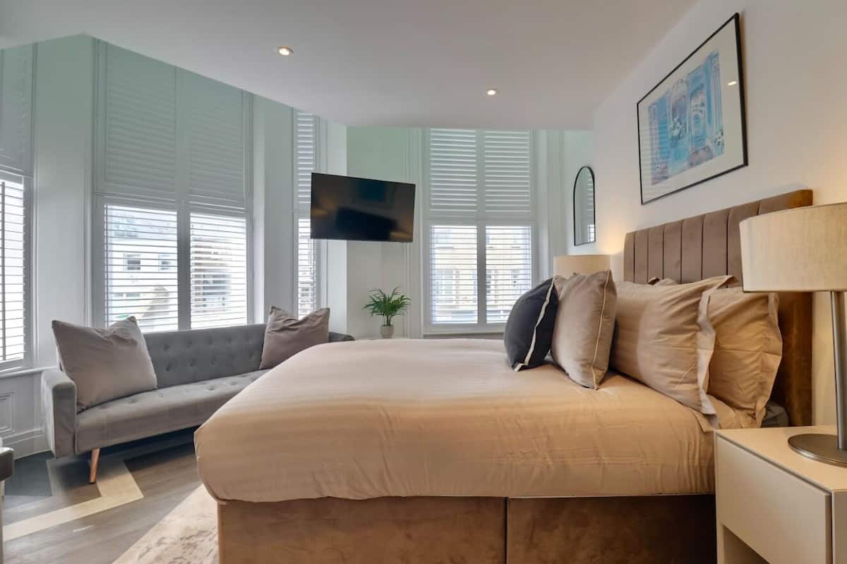 A bedroom with a large bed, a sofa, a TV, and a window with blinds.