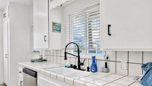 A kitchen with white cabinets, a black faucet, a dish soap bottle, and a window with blinds.