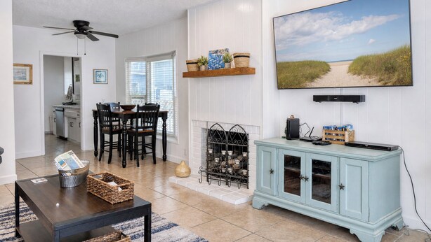 A living room with a TV, dining area, fireplace, and a view of the beach.