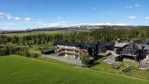 A large, multi-story building with a prominent staircase, surrounded by lush green fields and a mountainous backdrop. - Golsfjellet Apartment with Sauna (Gol)