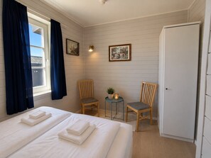 Une chambre d’hôtel avec un lit, deux chaises, une petite table avec une plante et une armoire blanche.