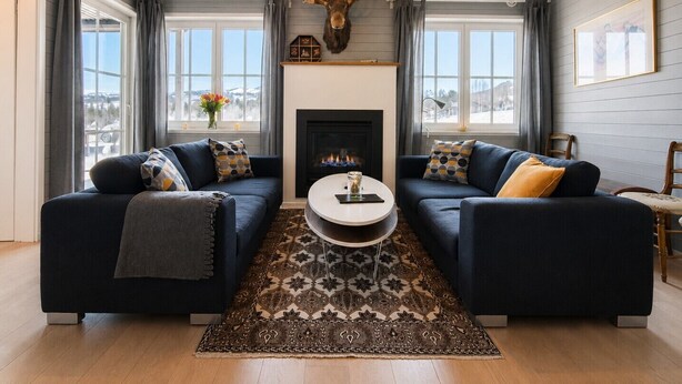 A living room with two sofas, a fireplace, a mounted deer head, and a view through large windows. - Golsfjellet Apartment with Sauna (Gol)