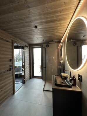 A modern bathroom with a wooden ceiling, a glass shower enclosure, a sink with a mirror, and a view of the outdoors.