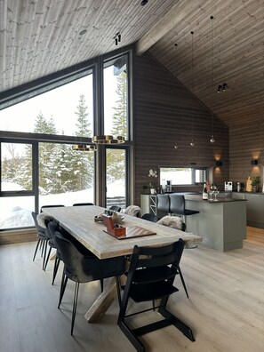 A modern interior with a large dining table, black chairs, and a kitchen area.