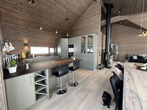 A modern kitchen with a central island, bar stools, a built-in oven, and a large window.