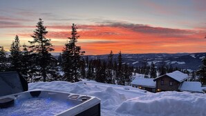 A hot tub in a snowy landscape with a view of a cabin and trees.