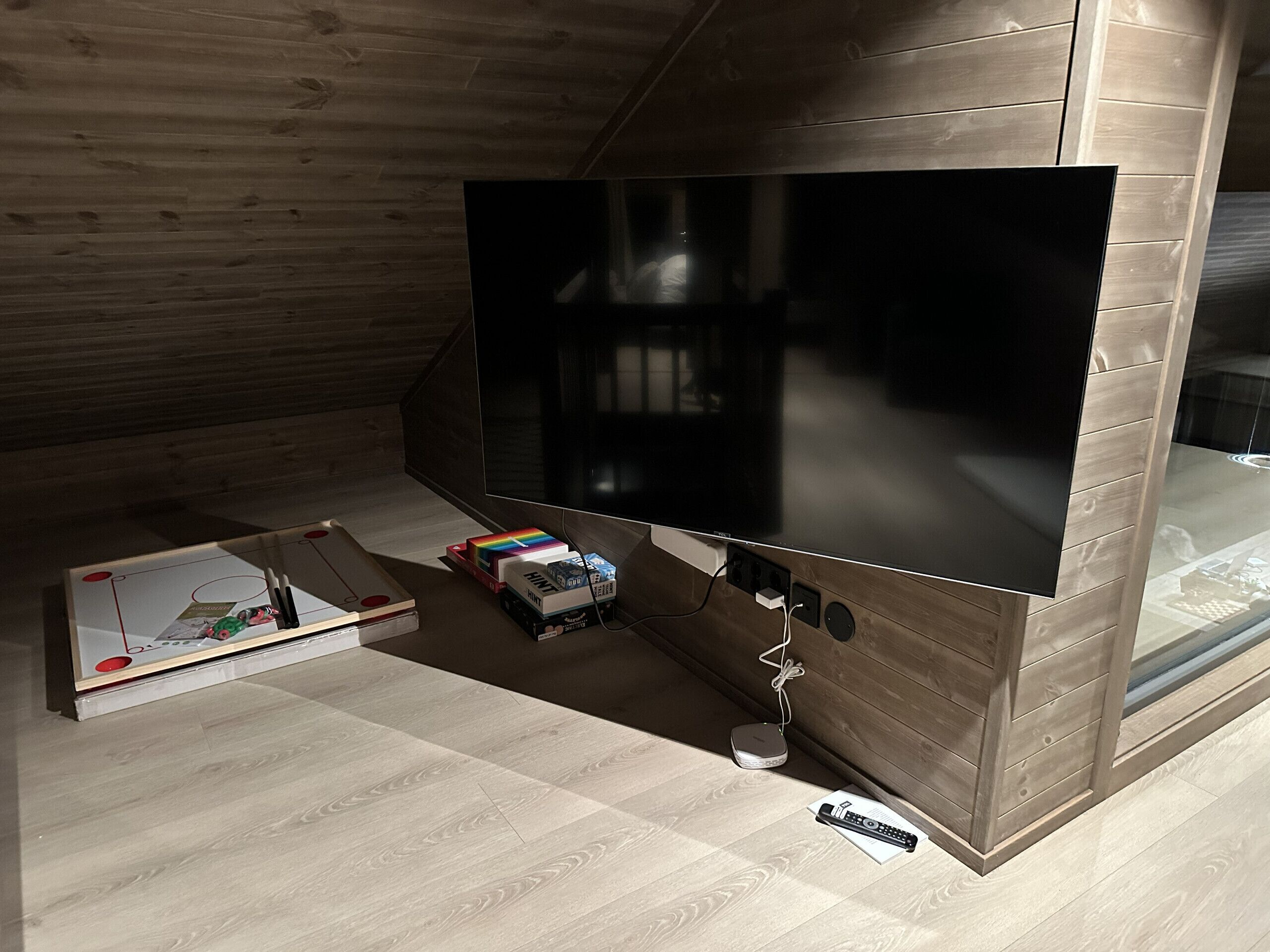 A modern room with a large flat-screen TV mounted on a wooden wall, a small table with a remote control, and a power strip on the floor.
