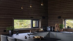 A modern kitchen with a central island, bar stools, a potted plant, and a window providing a view of greenery.