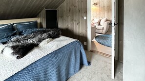 A bedroom with a large bed, a wooden ceiling, a door leading to a living area, and a light fixture.