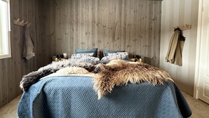 A bedroom with a wooden wall, a bed with a blue quilt, and a fur throw. - Newly renovated house close to everything (Hol)