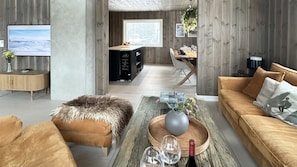 Una sala de estar moderna con un sofá, un reposapiés, una mesa de centro y un televisor.