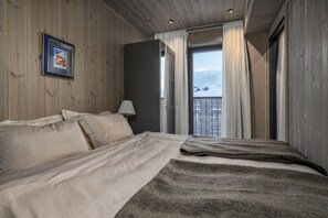 Un dormitorio con cama, mesita de noche, lámpara, un cuadro enmarco y una ventana con cortinas.