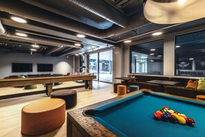 A pool table with balls, a billiards table, and seating areas in a modern indoor space.