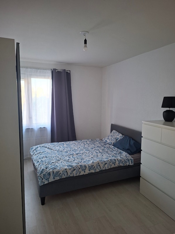 A bedroom with a bed, a dresser, a window with curtains, and a ceiling light.