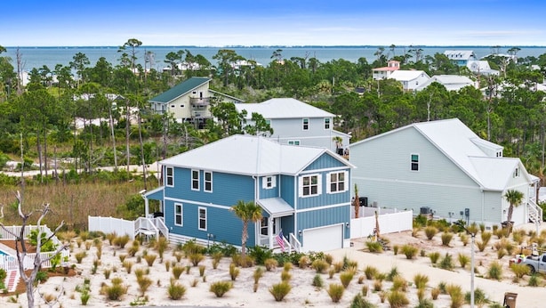 Una casa vista mare con un balcone, circondata da dune sabbiose e vegetazione.