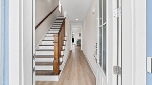 Un corridoio con una scala in legno, una porta con un pannello di vetro e un lampadario a soffitto.