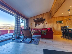 A room with a wooden interior, a red sofa, a dining table, and a mounted animal hide. - Spacious and central apartment in Ustaoset (Hol)