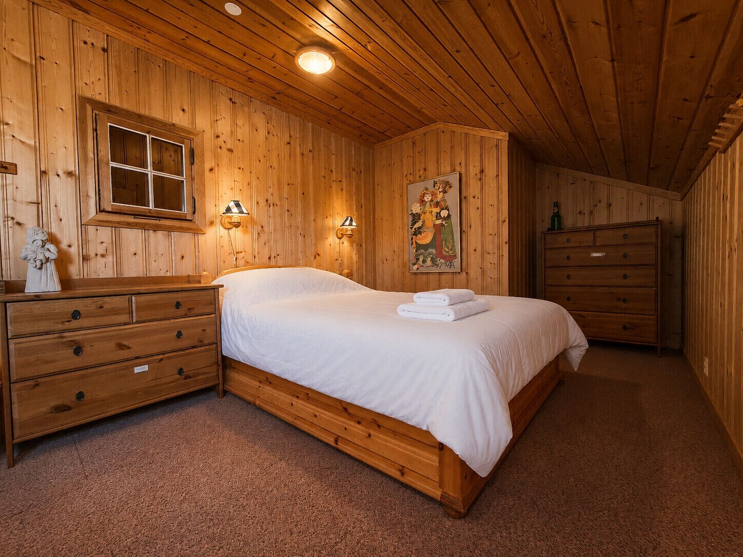 A wooden-paneled room with a bed, a dresser, a nightstand, and a painting on the wall.