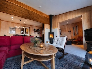 Una sala de estar acogedora con detalles de madera, una mesa redonda de madera, un sofá rojo, un sillón blanco y una chimenea.