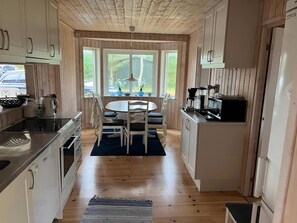 Eine Küche mit Holzausstattung, einem Esstisch mit Stühlen und Blick ins Freie durch große Fenster.