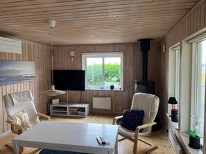 Ein gemütliches Zimmer mit Holzwänden, einem großen Fenster, einem Flachbildfernseher, einem weißen Sofa, einem Couchtisch und einem Kamin.
