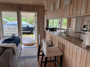 Innenansicht einer Holzhütte mit Bett, Bar und Blick auf ein Auto draußen.